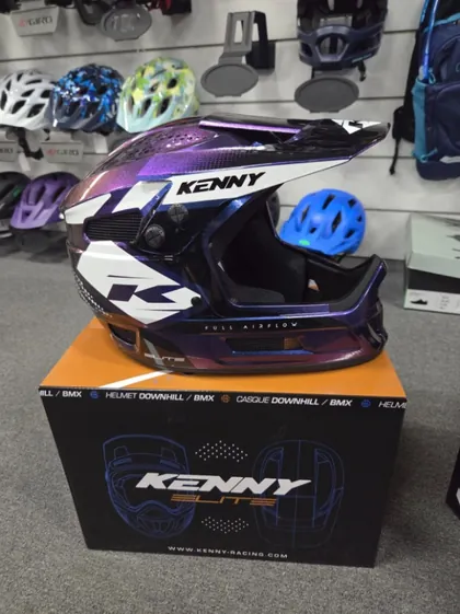 A purple Kenny Elite full-face helmet on its box in front of the helmet wall
