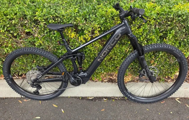 A black Norco electric mountain bike against a hedge